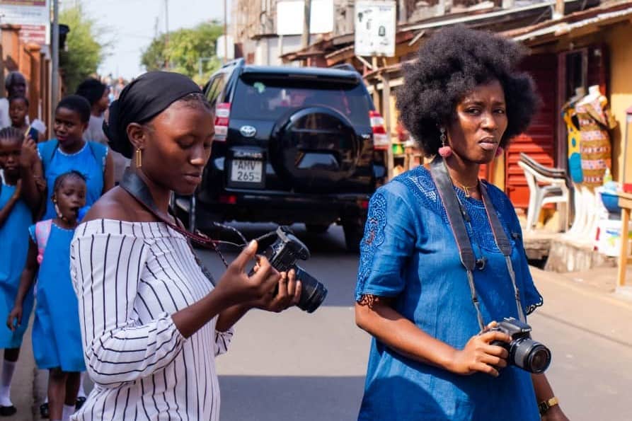 2 woman with professional cameras cross a road in Sierra Leone