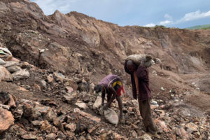 two men stand on a rocky mountain side mining for cobalt