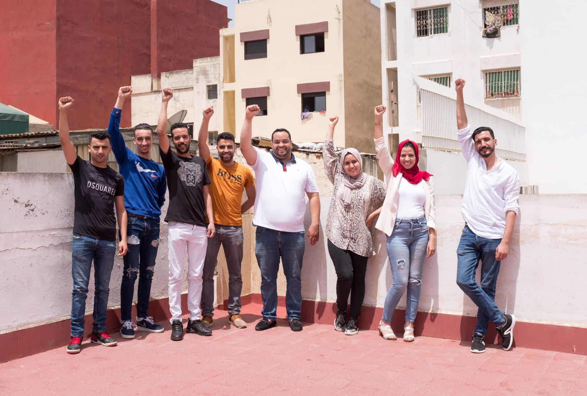 a small group of activists in Morocco stand outside their office, fists raised in victory