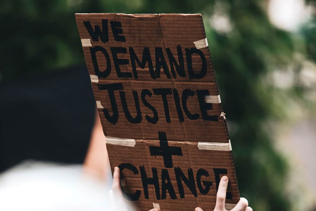 At a protest, a sign written on cardboard reads, "We demand justice + change."
