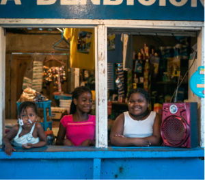 Three kids from Honduras the coast stand in a small shop smiling. Help us support activists to improve the lives of communities like this.