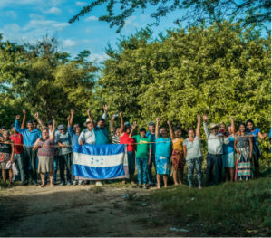A long line of people raising their fists into the air while holding a Honduras flag. Support activists like these today.