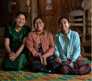 Three smiling women from Myanmar sitting on the floor. When you donate, you support activists like these.