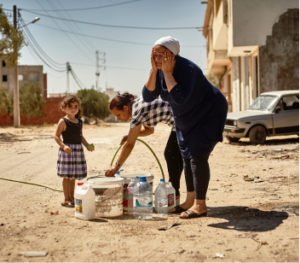 Two women and a child wash their faces in a dusty street in Tunisia. Donate to support activists like these.