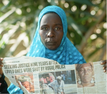 A woman wearing a light blue hijab holds a paper with the headline 'seekng justice nine years after loved ones were shot by rogue police'. Help us support activists for justice.