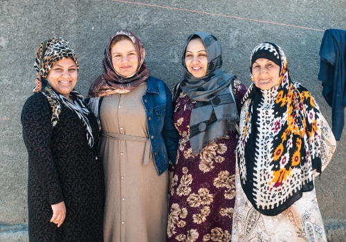 Four women wearing colourful hijabs stand side-by-side in front of a wall.