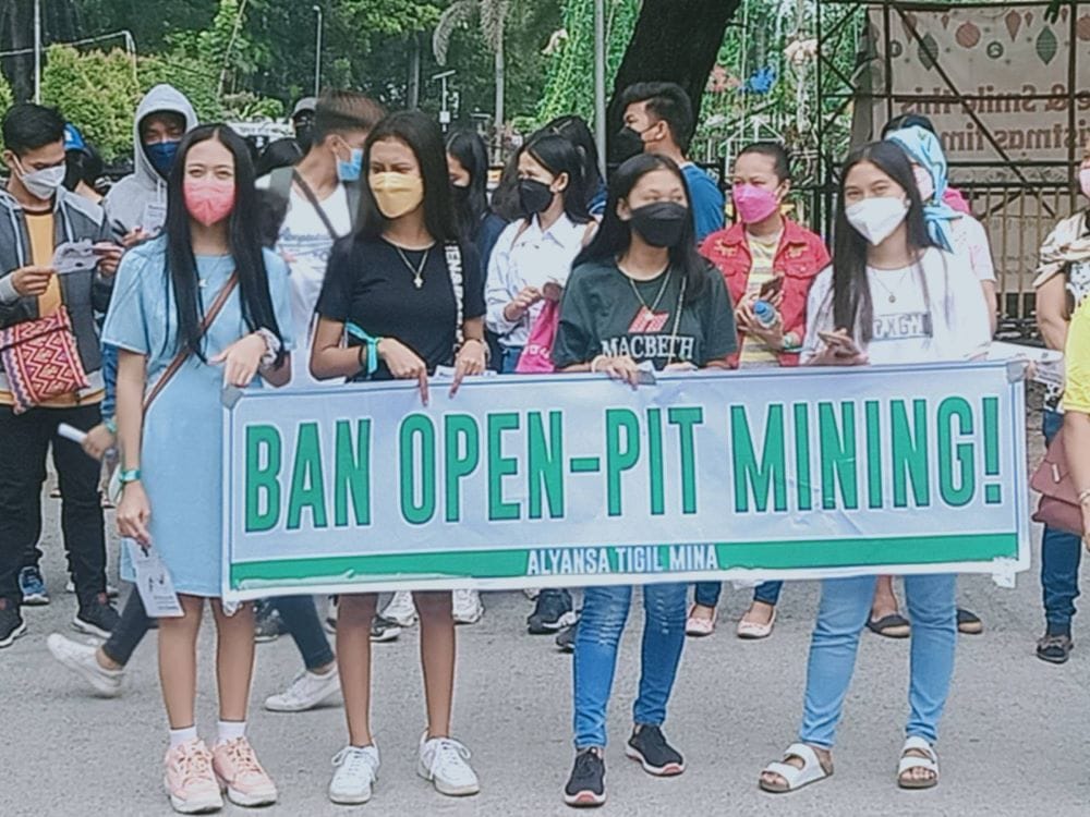 A group of women at a protest hold a sign reading ban open-pit mining