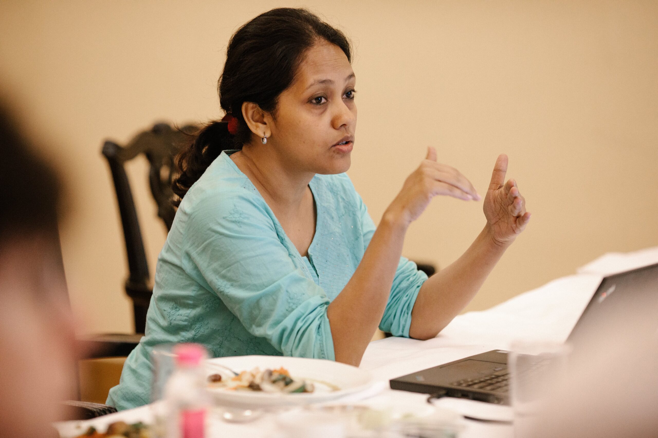 A young Indian woman in light green top and ponytail speaks at a table during a meeting