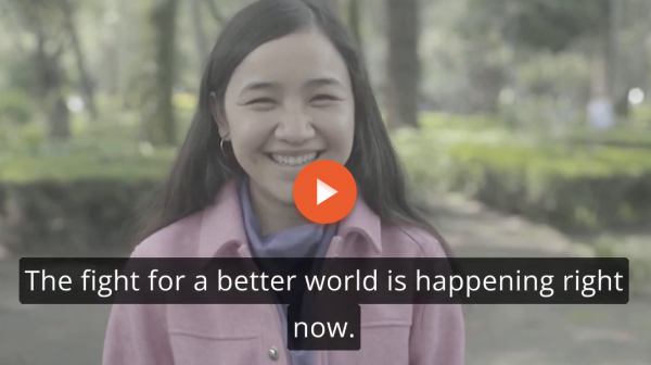A young woman with dark hair wearing a pink jacket smiles. A video play button appears above a caption: the fight for a better world is happening right now.