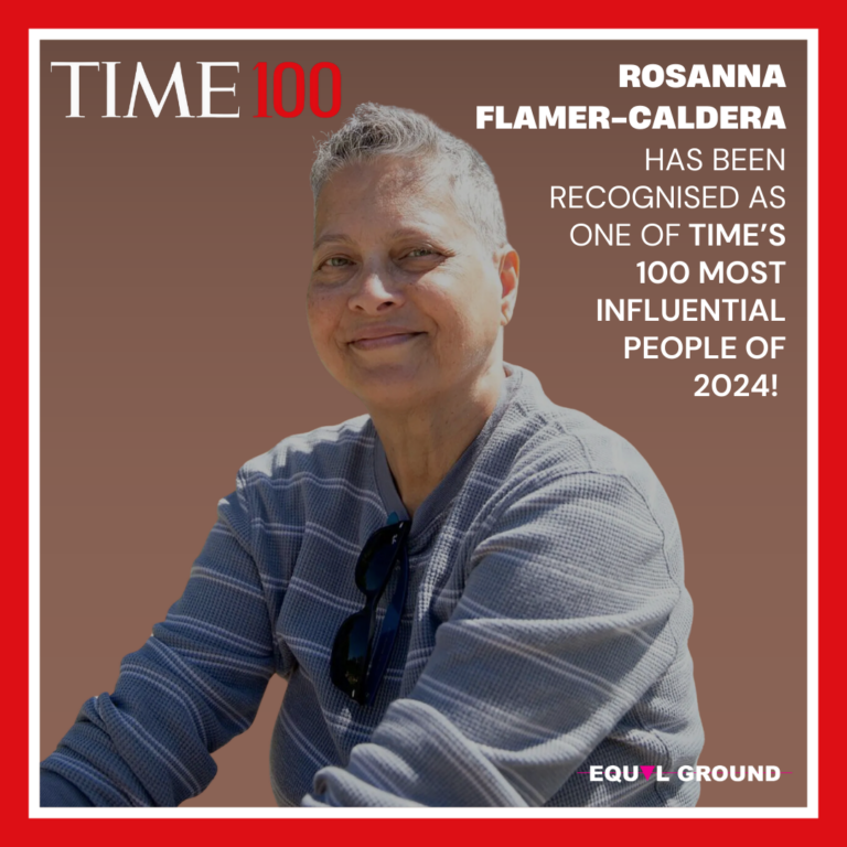 Rosanna is seated within a red Time100 frame. She sports cropped grey hair and long sleeve shirt