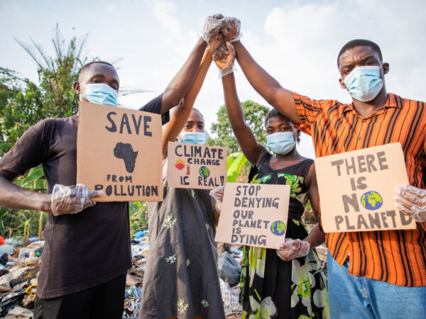 Four Young Adults Protest With Signs Against Pollution Outside An Illegal Open Landfill In Africa.