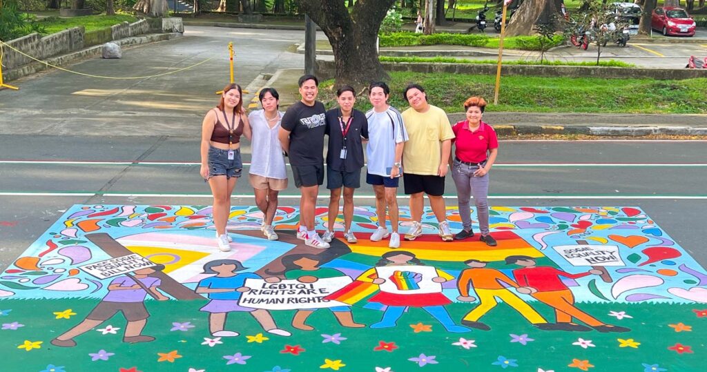 LGBTQ+ rights activists standing on a mural about the SOGIE Equality Bill in the Philippines