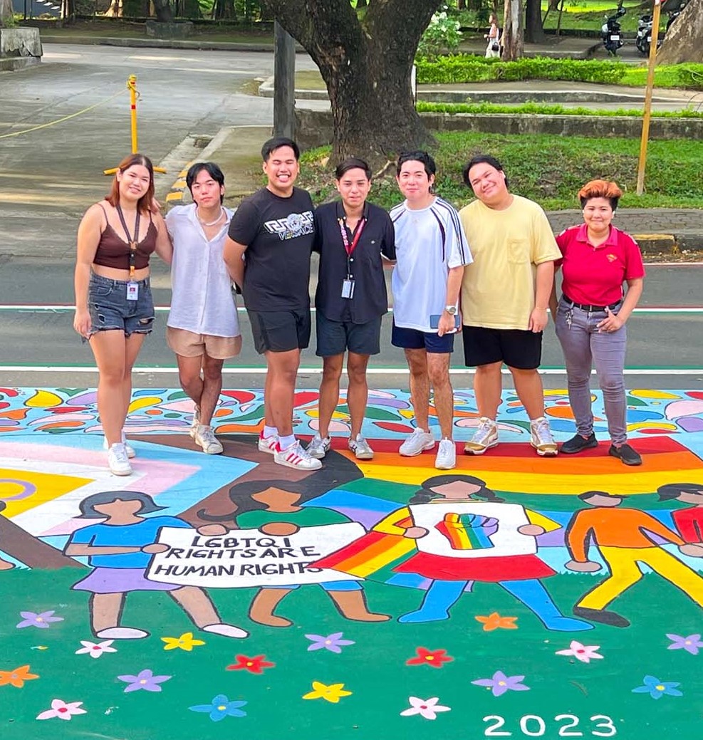 A group of student LGBTQ+ rights activists in the Philippines standing on a mural about the SOGIE Equality Bill.