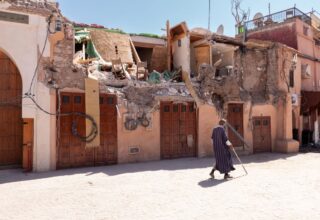 A Man In Dark Clothing With A Walking Stick Passes Homes Damaged By The Earthquake In Morocco