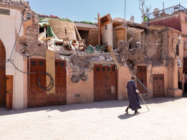 A Man In Dark Clothing With A Walking Stick Passes Homes Damaged By The Earthquake In Morocco