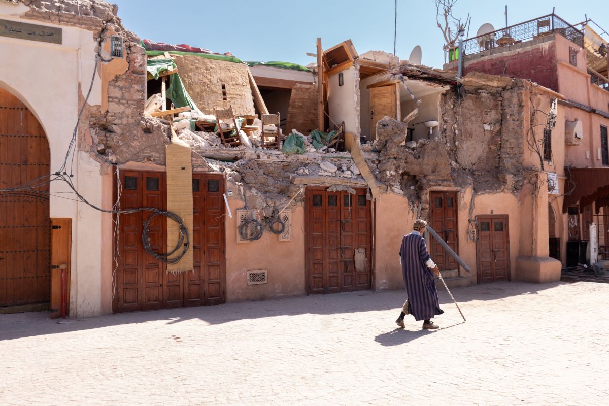 A man in dark clothing with a walking stick passes homes damaged by the earthquake in Morocco