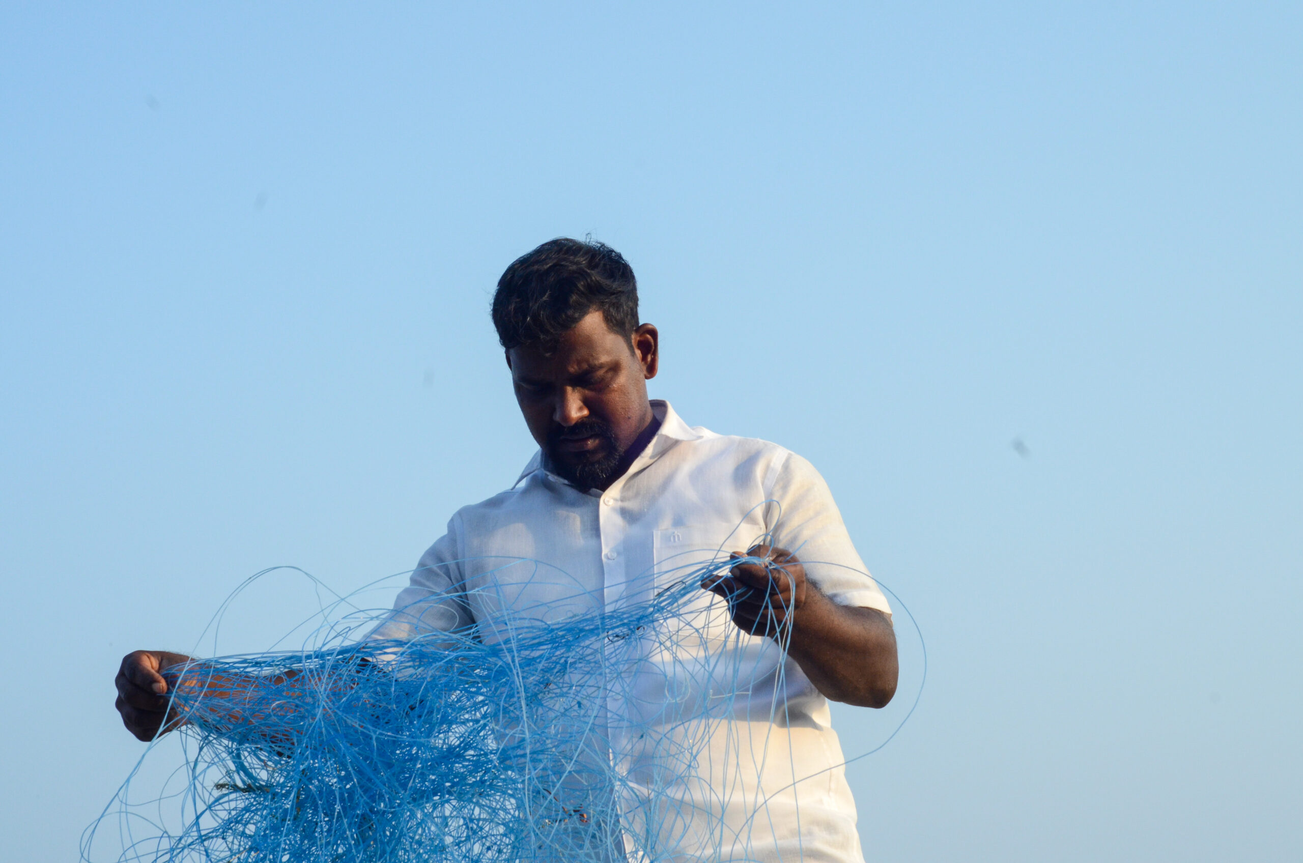 A fisherman untangles his nets against a blue sky.